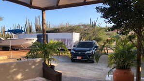 A covered outdoor area with a white boat, a black car, and a wicker sofa.