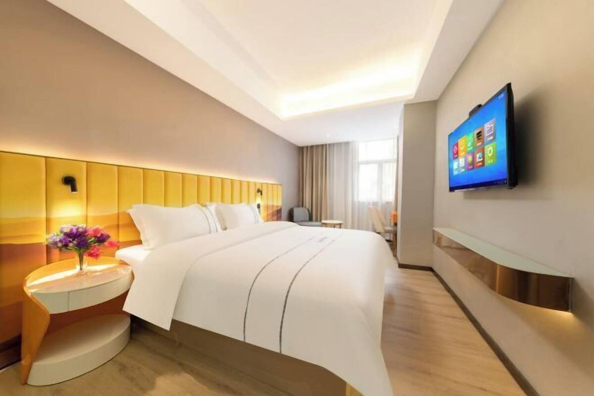 Ein modernes Hotelzimmer mit Bett, einem an der Wand befestigten Fernseher und einem Nachttisch mit Blumen.