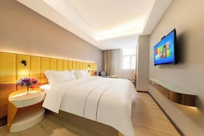 A modern hotel room with a bed, a TV mounted on the wall, and a bedside table with a vase of flowers.