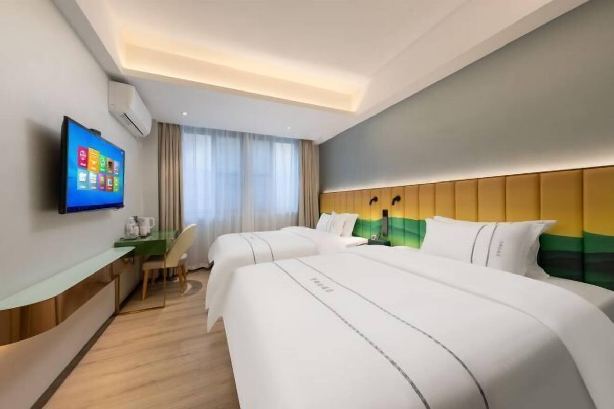 Ein Hotelzimmer mit zwei Betten, einem Schreibtisch mit Stuhl, einem Flachbildfernseher und einem Fenster mit Vorhängen.
