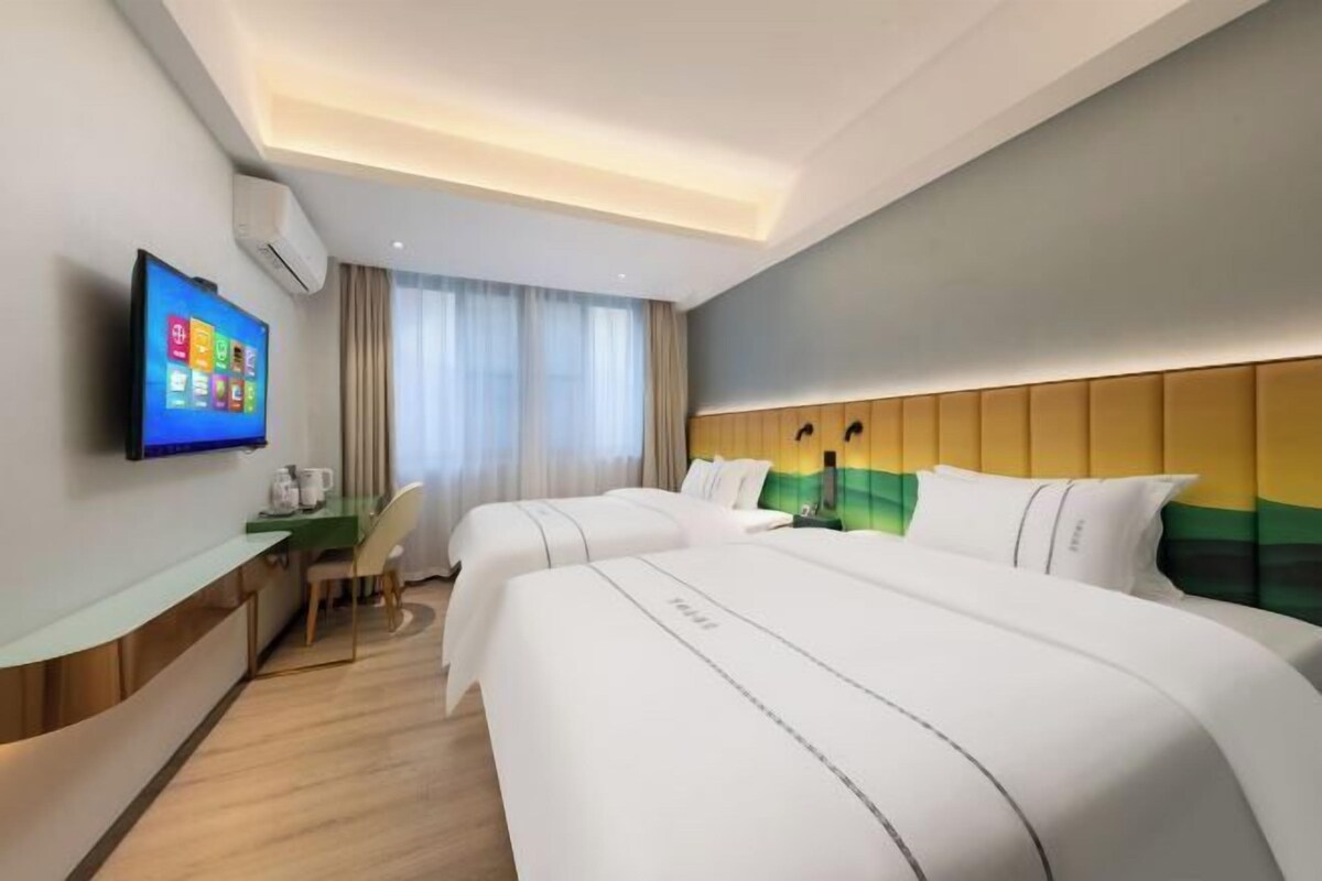 A hotel room with two beds, a desk, a flat-screen TV, and a window with curtains.
