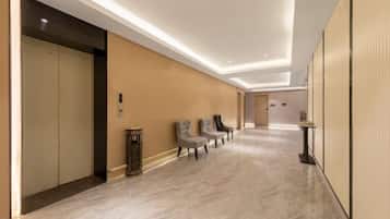A hotel hallway with a marble floor, a reception desk, and a row of chairs.