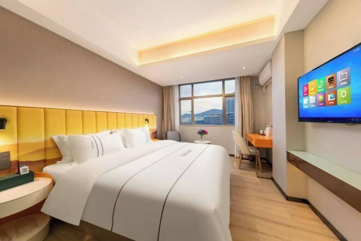 Ein Hotelzimmer mit einem Bett, einem Schreibtisch, einem Stuhl, einem Fernseher und einem Fenster mit Blick auf die Stadt.