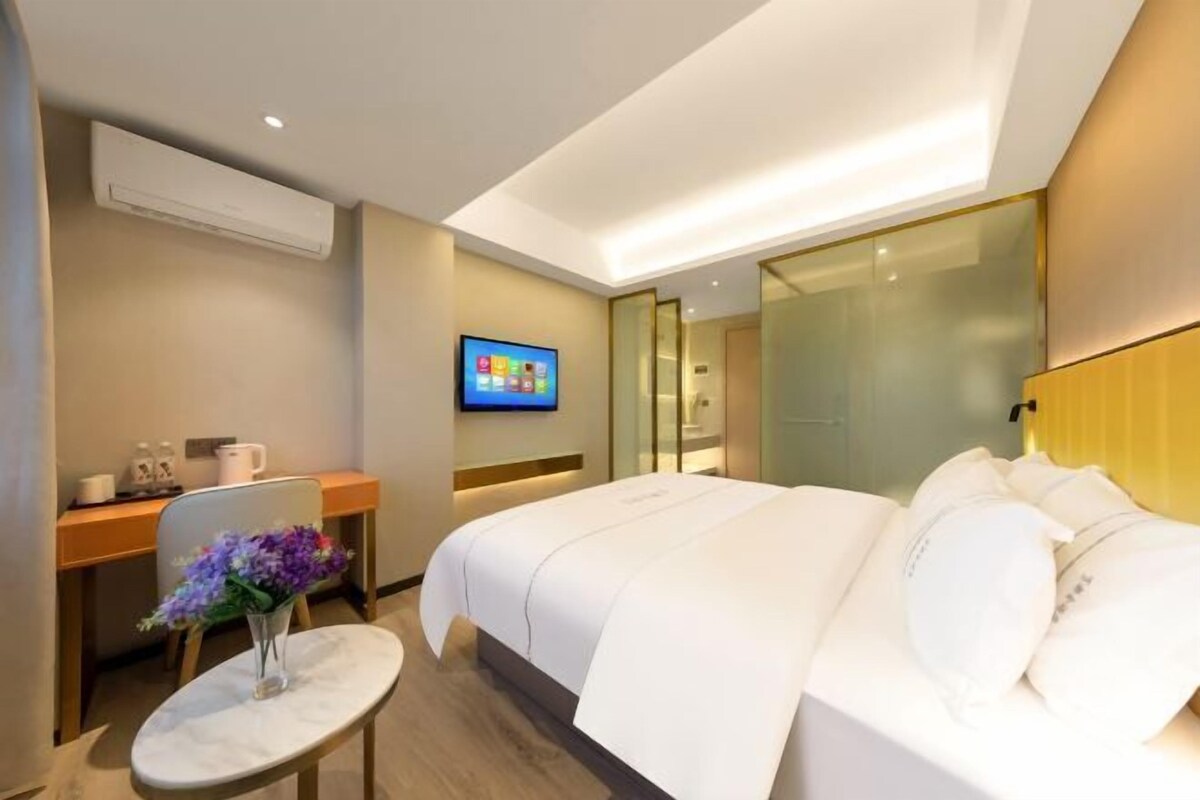 A modern hotel room with a bed, a desk, a TV, and a small table with flowers.