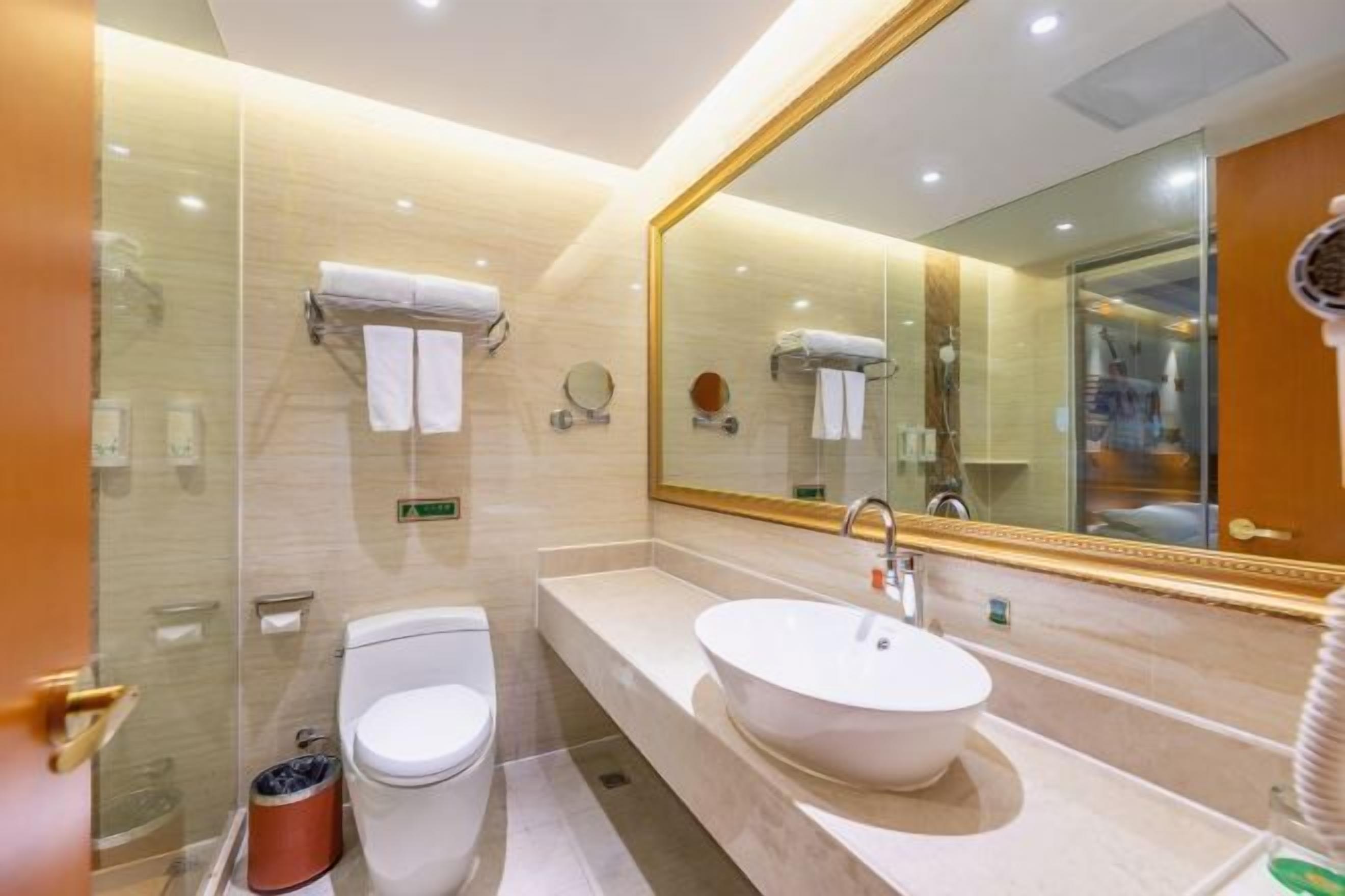 A modern bathroom with a glass shower enclosure, a white toilet, a large oval sink, and a mirror with a gold frame.