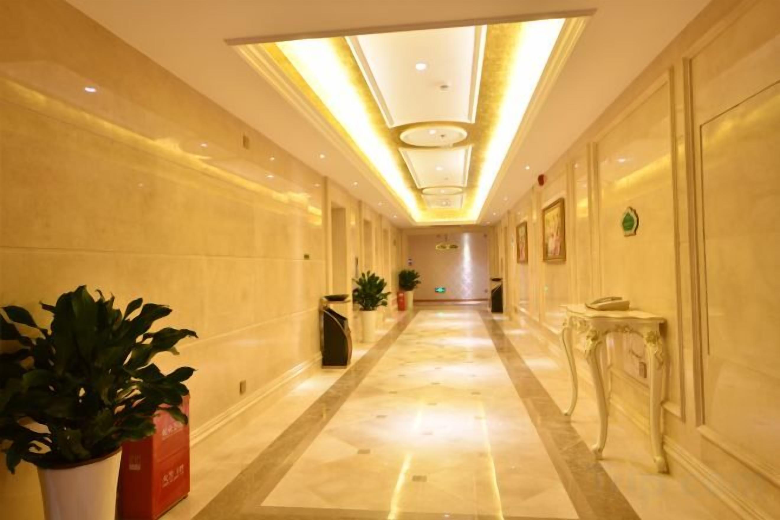 A hotel corridor with a marble floor, potted plants, and a reception desk.
