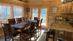A wooden cabin interior with a dining table, chairs, a kitchen island, and large windows. - Beautiful New Cabin on the Broad River, 3 miles from Lake Lure, NC (Lake Lure)