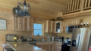 A spacious kitchen with wooden cabinets, a large island with bar stools, stainless steel appliances, and a hanging light fixture. - Beautiful New Cabin on the Broad River, 3 miles from Lake Lure, NC (Lake Lure)