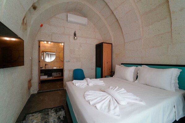 A hotel room with a large bed, a bathroom with a mirror, and a wooden cabinet. - The Niche Cave Hotel (Nevsehir)