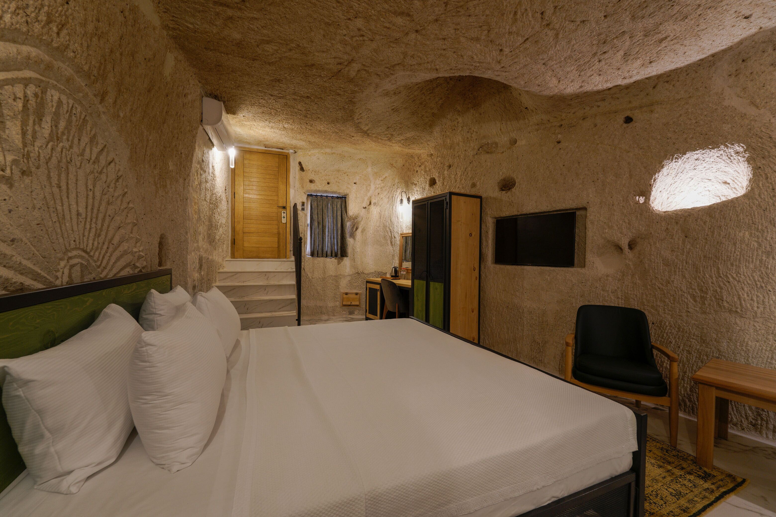 Una habitación con cama, sillón, escritorio y televisor.