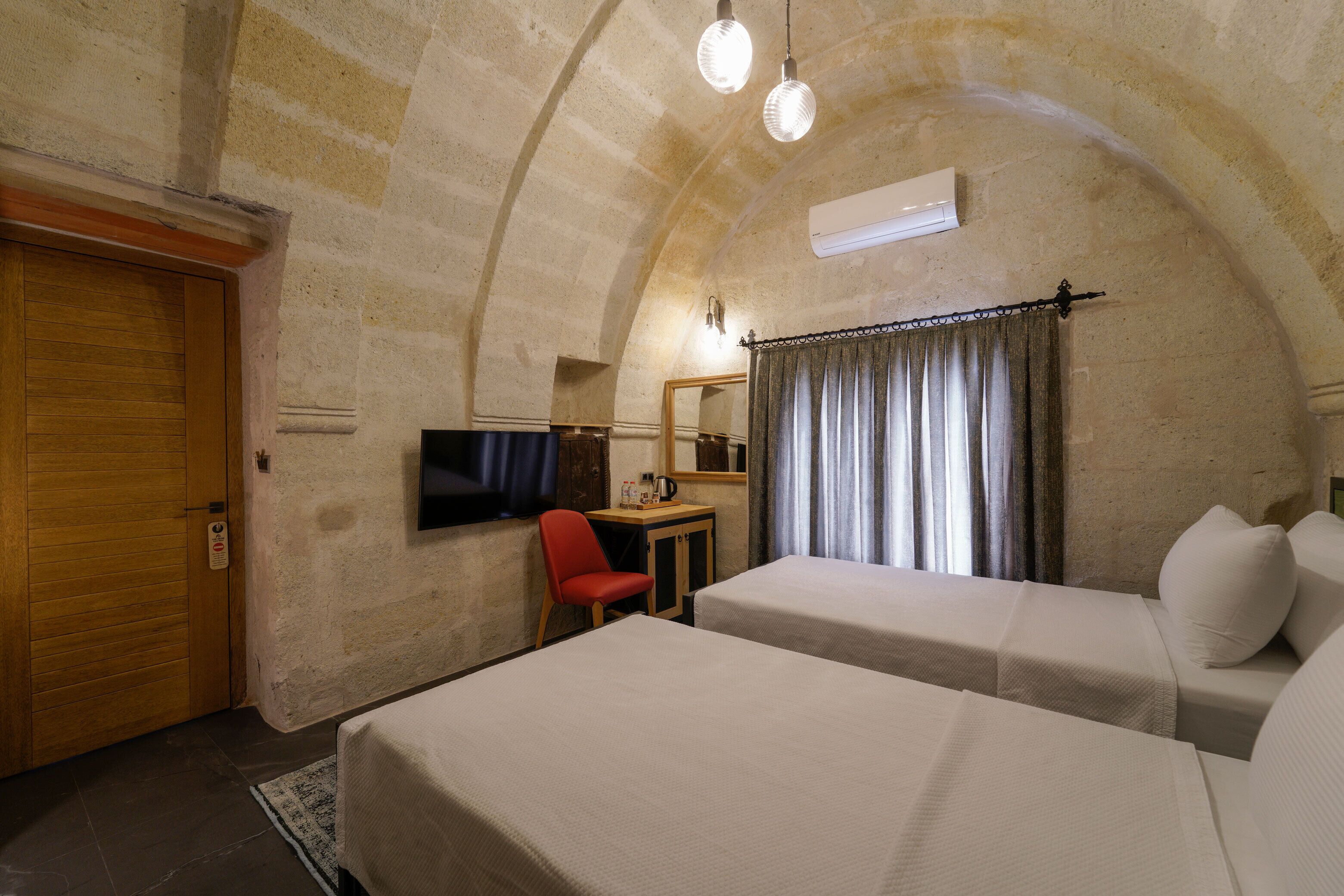 A room with two beds, a wooden door, a small table with a TV, and a red chair.