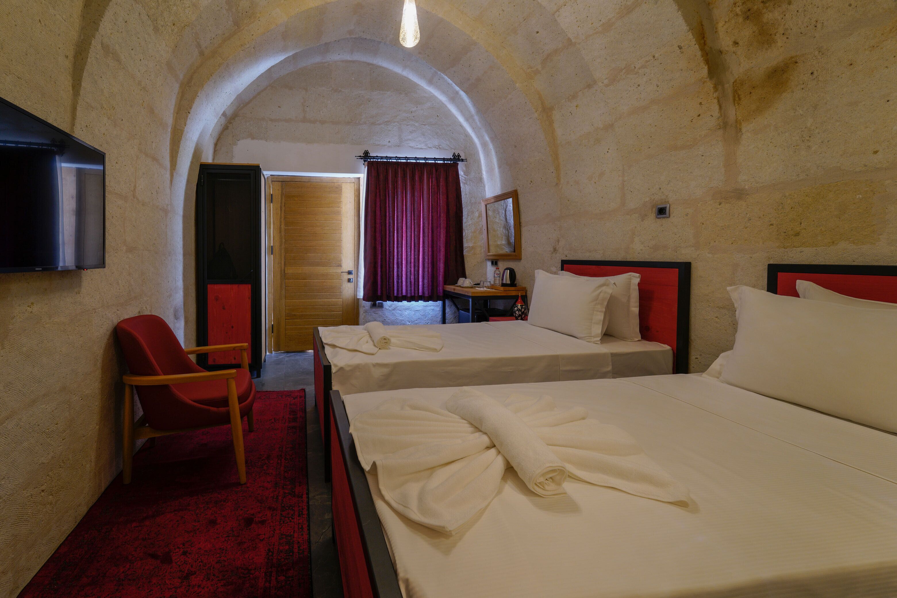 Habitación de hotel con dos camas, un televisor, una silla roja y una puerta de madera.