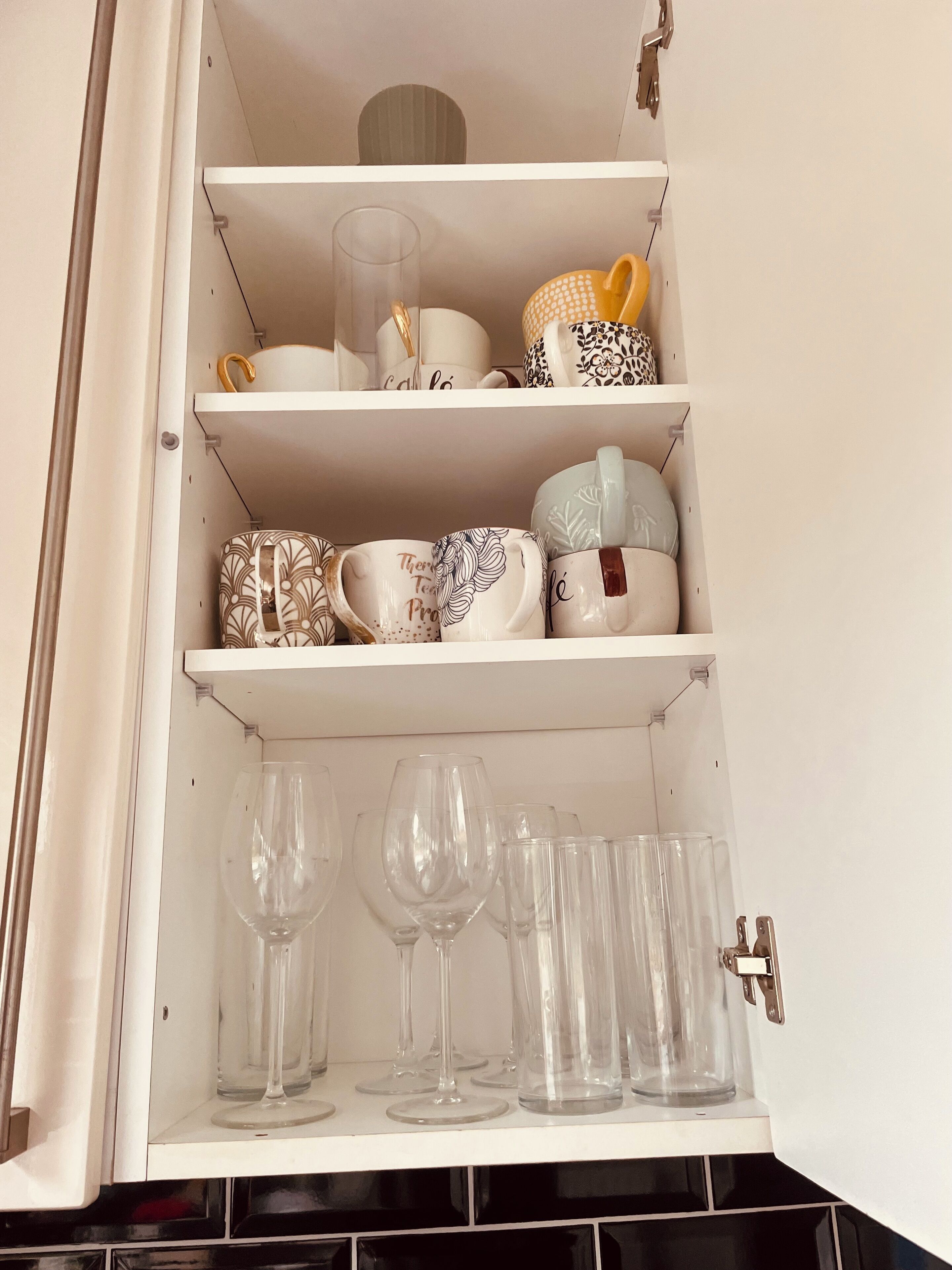 A kitchen cabinet with shelves holding various kitchenware and glassware.