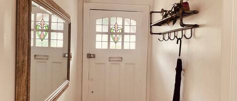 A hallway with a white door, a mirror, and a wall-mounted rack with an umbrella.