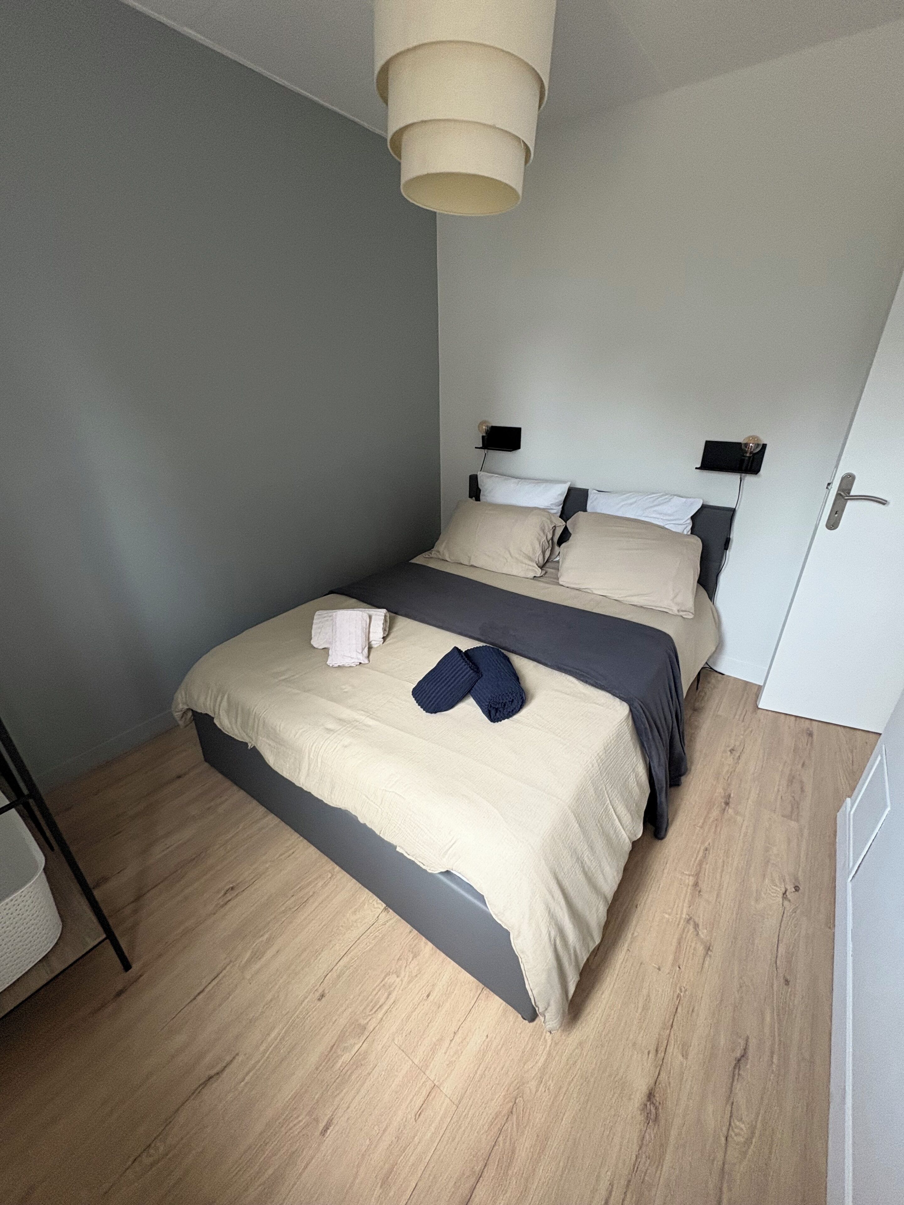 Een slaapkamer met een bed, nachtkastjes, een hanglamp en een deur.
