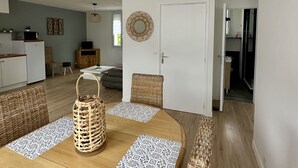 A modern living room with a wooden dining table, wicker chairs, and a hanging light fixture.