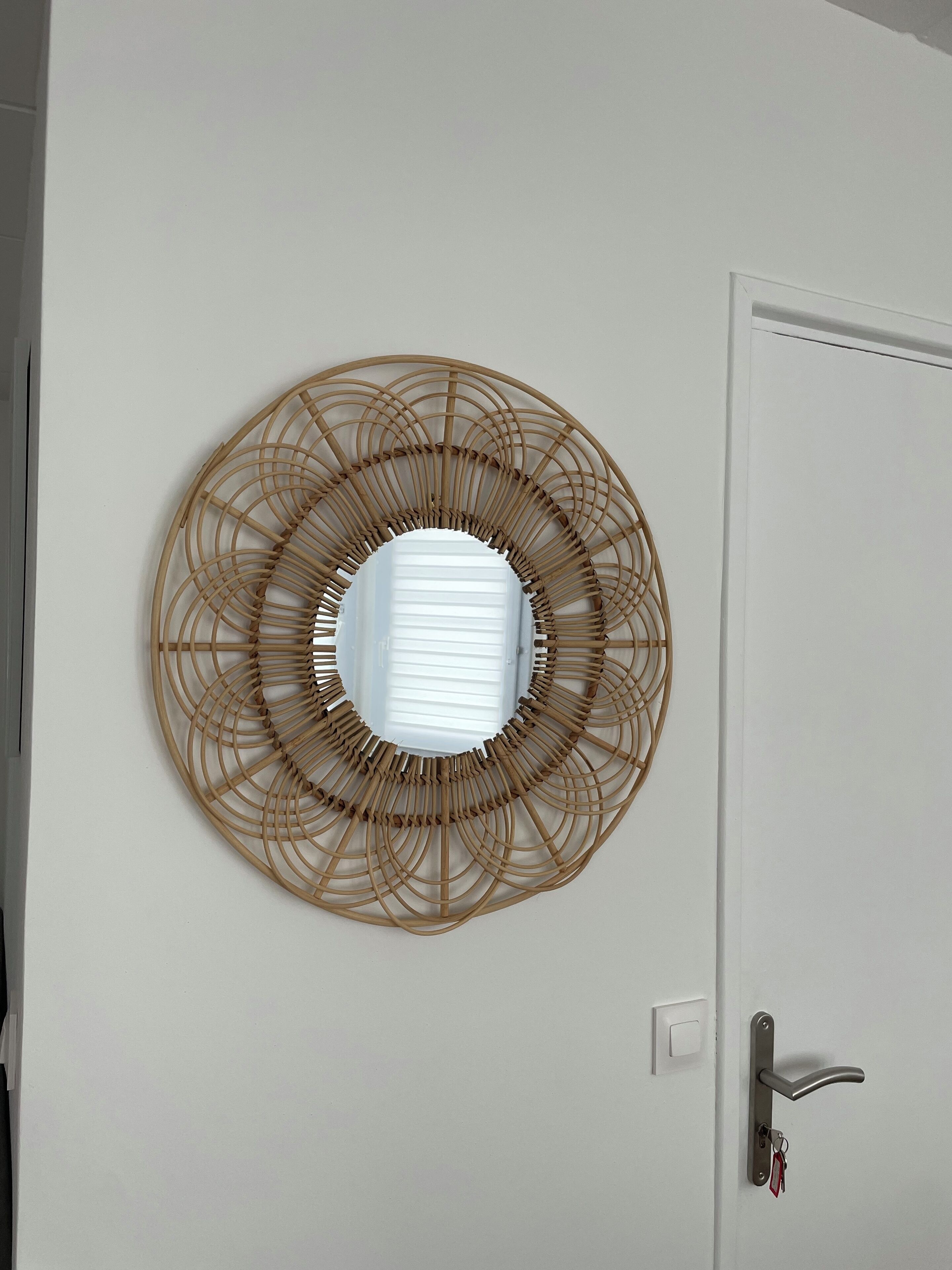 A circular woven wall art piece centered on a white door with a modern handle and keychain.
