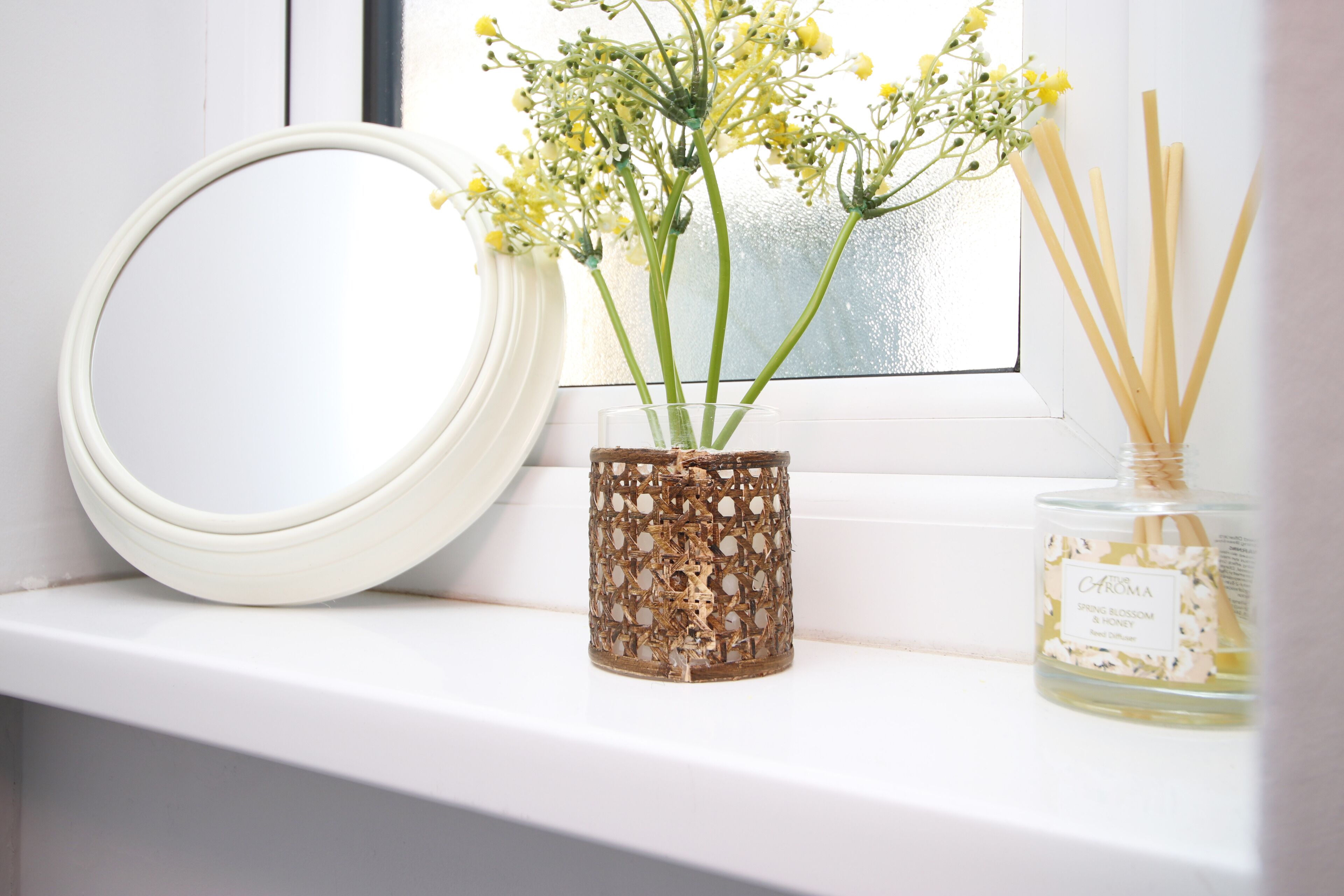 A window sill with a white mirror, a decorative vase with flowers, and a bottle of fragrance.