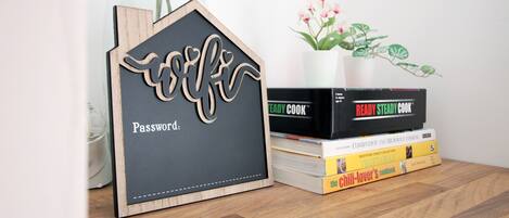 A wooden house-shaped password holder with a plant and cookbooks on a wooden surface.
