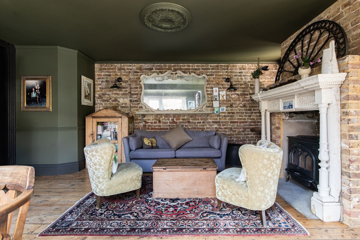 A cozy living room with a brick wall, a fireplace, a sofa, two armchairs, a wooden coffee table, and a patterned rug.