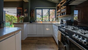 A modern kitchen with white cabinets, a large stove, and a window overlooking a garden. - Beautiful and spacious Edwardian home by the seaside (Worthing)