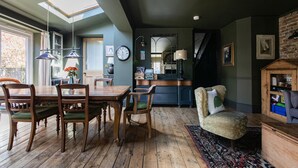 A dining area with a wooden table and chairs, a kitchen in the background, and a cozy seating area with a patterned rug. - Beautiful and spacious Edwardian home by the seaside (Worthing)