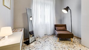 A room with a white desk, a brown sofa, a standing lamp, a mirror, and a window with sheer curtains. - BDC - Termini Studio (Roma)