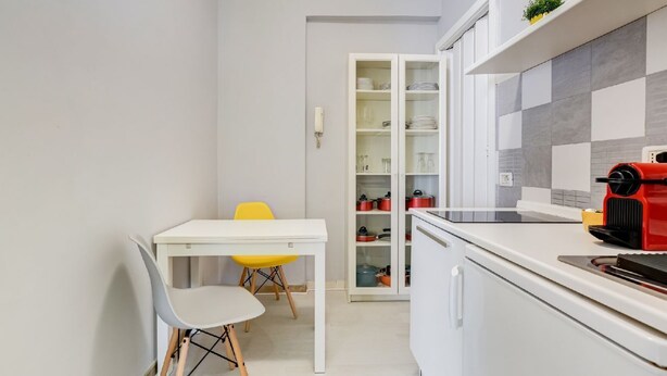 A compact kitchen with a white table, a yellow chair, and a cabinet with dishes and pots. - BDC - Termini Studio (Roma)