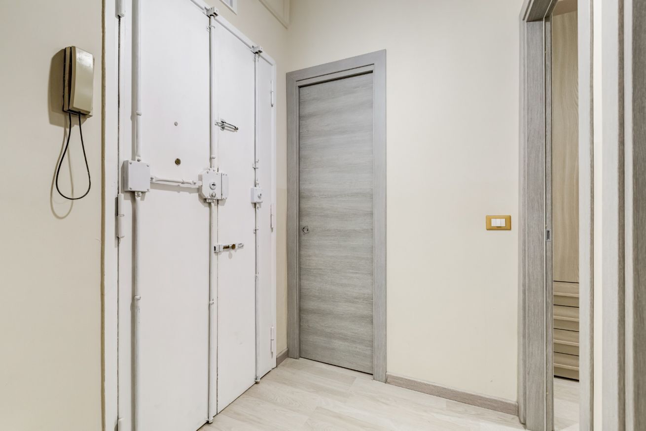 A hallway with a white door, a grey door, and a wall-mounted intercom.