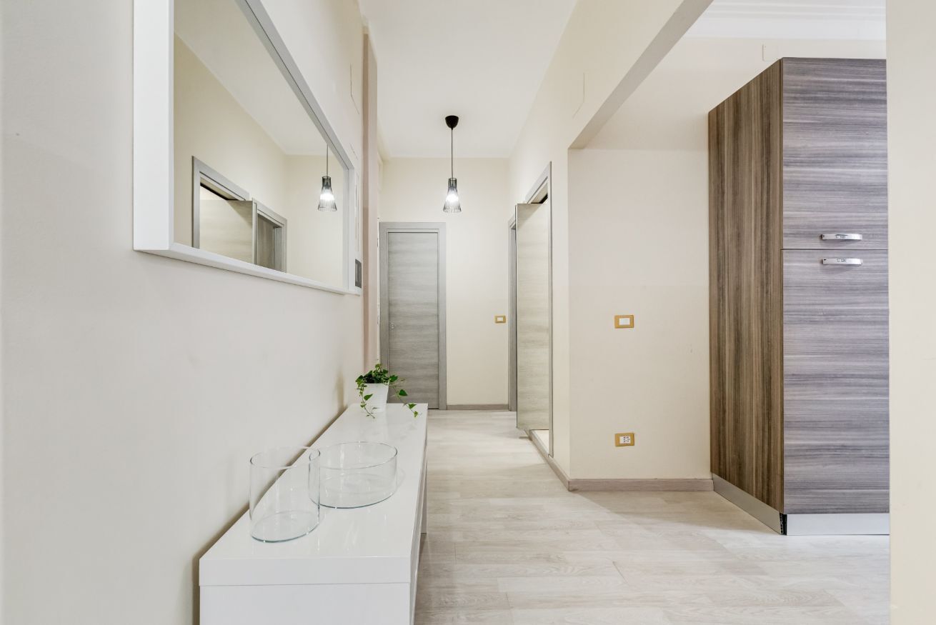 Un couloir avec une coiffeuse blanche, un miroir, des luminaires suspendus et une armoire.