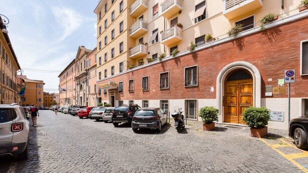 Una calle adoquinada flanqueada por automóviles estacionados y edificios de varios pisos con balcones.