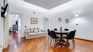 A dining area with a round table and chairs, a sofa, and a framed picture on the wall.
