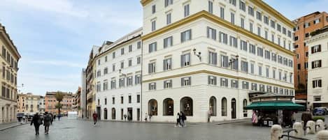 A historic building with a central courtyard, arched doorways, and a street-side kiosk.