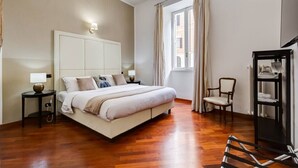 A bedroom with a large bed, bedside tables, a chair, a window with curtains, and a bookshelf.