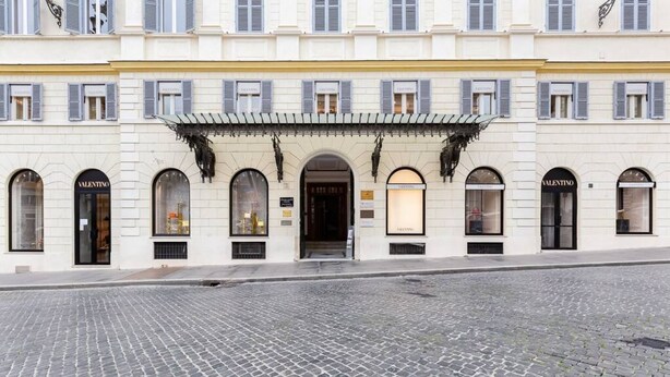 A building with arched windows and a central entrance, featuring storefronts with signage.