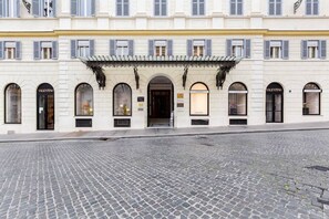 A building with arched windows and a central entrance, featuring storefronts with signage. - BDC - Spanish Steps Gold 2bdr suite (Roma)
