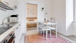 A compact kitchenette with a microwave, sink, and stove, a small dining area with a table and chairs, and a bed in the adjacent room. - BDC - Termini Sunrise Apartment (Roma)