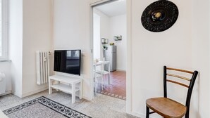 A living room with a TV, a white bench, a patterned rug, and a dining area in the background. - BDC - Termini Sunrise Apartment (Roma)