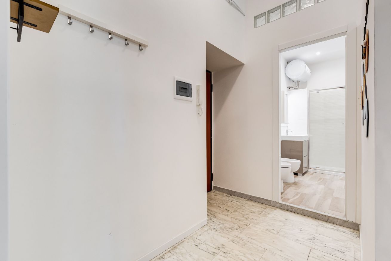 A hallway with a marble floor, a white wall, and a door leading to a bathroom.