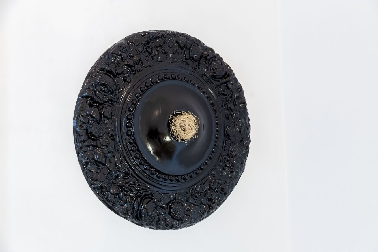 Un objet circulaire noir, orné et richement décoré de motifs floraux complexes, avec un élément métallique au centre.