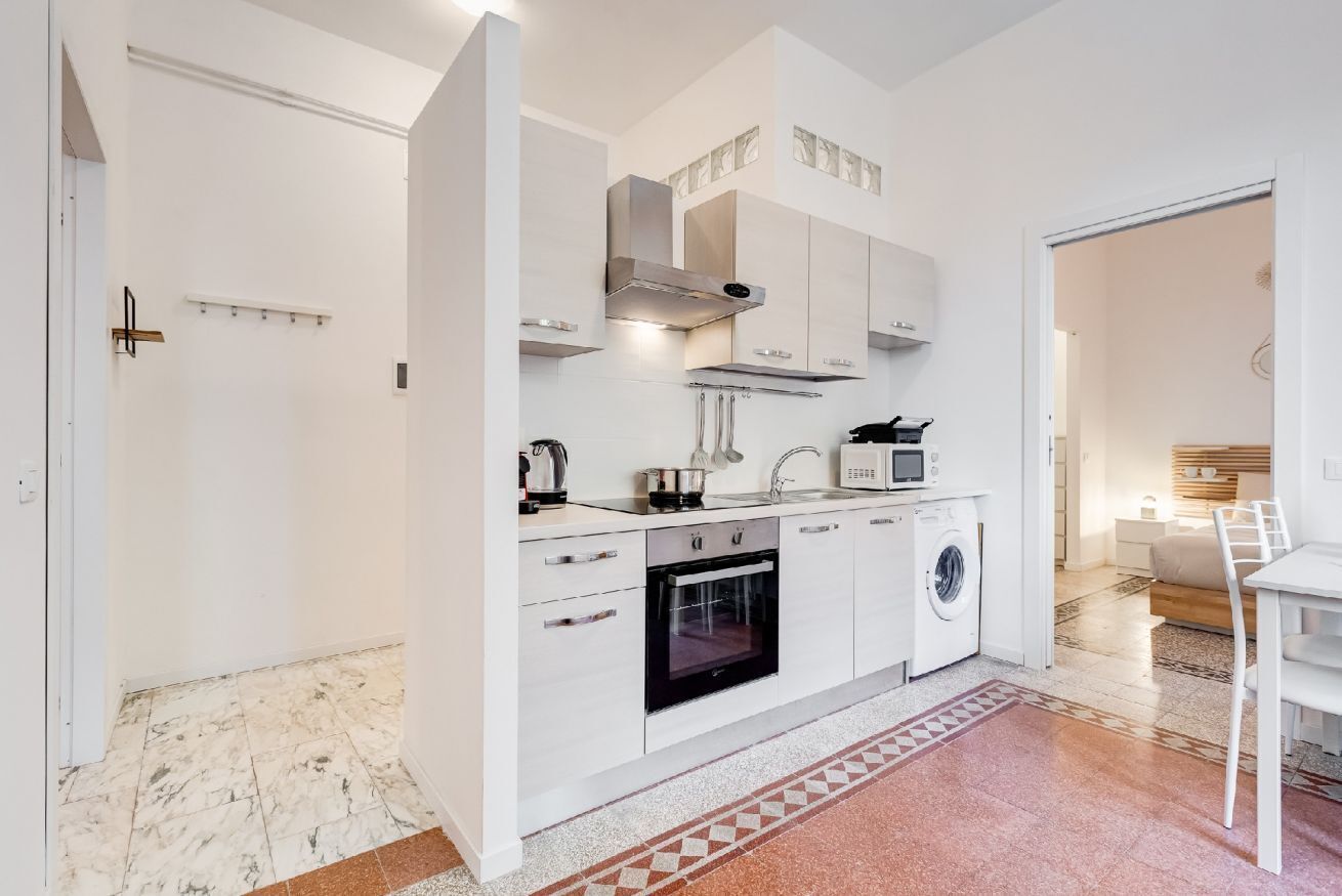 A compact kitchen with white cabinets, a microwave, an oven, and a washing machine.