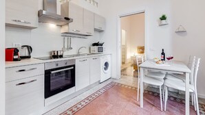 A compact kitchen with a microwave, oven, and washing machine, a dining area with a table and chairs, and a small plant on the wall. - BDC - Termini Sunrise Apartment (Roma)