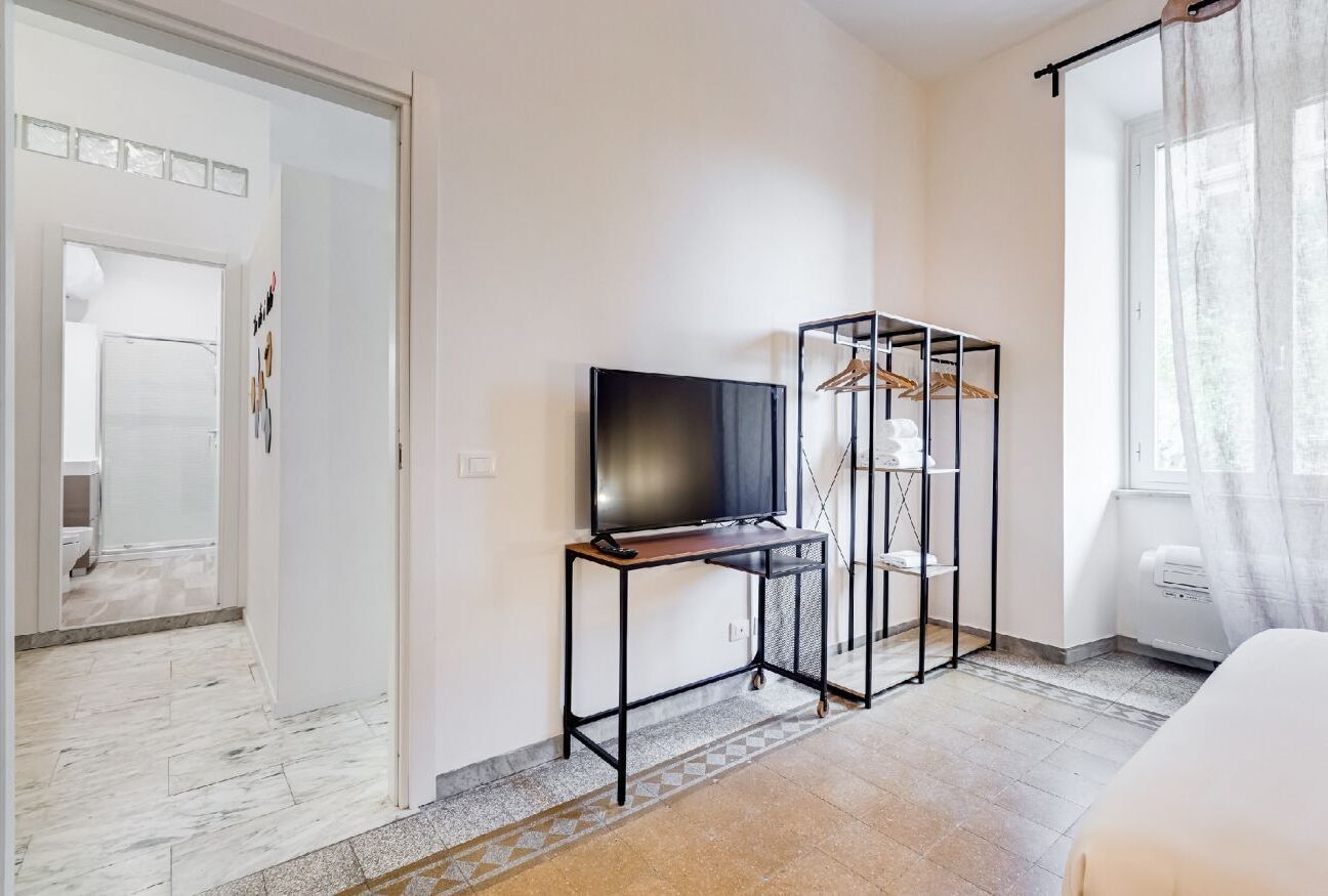 A room with a TV on a stand, a coat rack, and a bed.