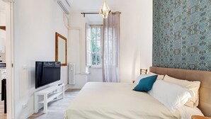 Une chambre à coucher avec un lit, une télévision, une fenêtre avec des rideaux, un mur à motifs et un luminaire suspendu.