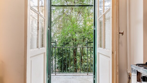Un couloir étroit mène à un balcon doté d’une rambarde en métal, d’où l’on peut admirer la vue sur les arbres, et une porte se trouve sur la droite.