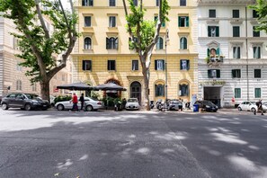 Una veduta di strada con un edificio giallo, auto parcheggiate e un albero.