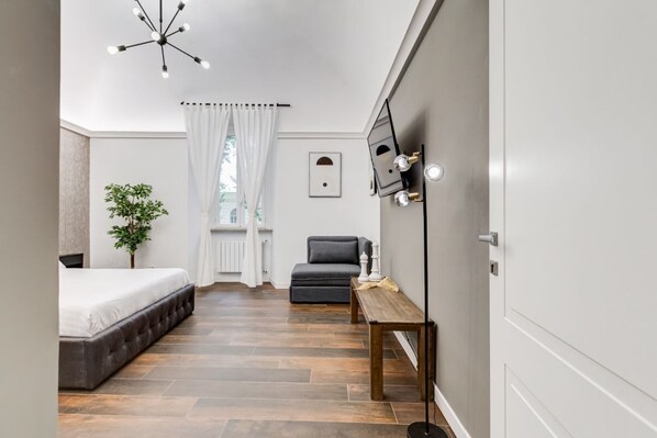 Camera da letto moderna con un letto, un divano grigio, un tavolino, una pianta e un lampadario.