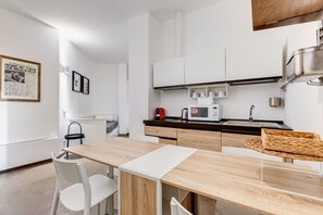 A modern kitchen with white cabinetry, a wooden dining table, and a microwave.
