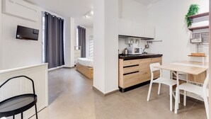 Moderni huoneisto, jossa on pieni keittiö, ruokailutila, seinälle asennettu televisio ja sängyllä varustettu makuuhuone.
