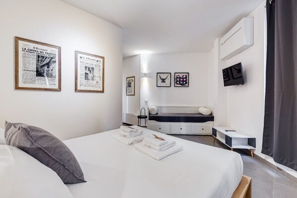 A modern hotel room with a bed, a bedside table, a flat-screen TV, and framed pictures on the wall.